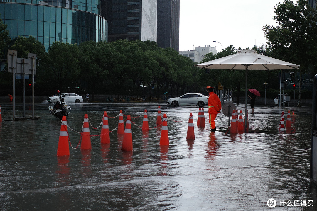 一名环卫工人在会展中心门口躲雨，衣服和路障在积水的倒映下相映成趣