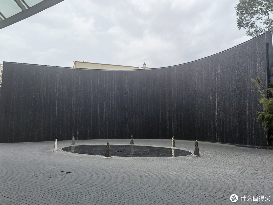大门入口处的正对面是一个环状的黑色外墙组成的小人工瀑布，上面的水顺着流下