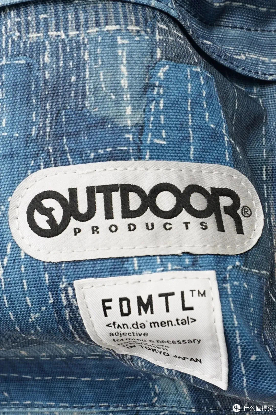 OUTDOOR PRODUCTS 联名 FDMTL背包 使用了 FDMTL 标志性的厚靛蓝染提花面料，整体呈现出一种斑驳的质感，随着时间推移，更会逐渐呈现出独特的色落质感。