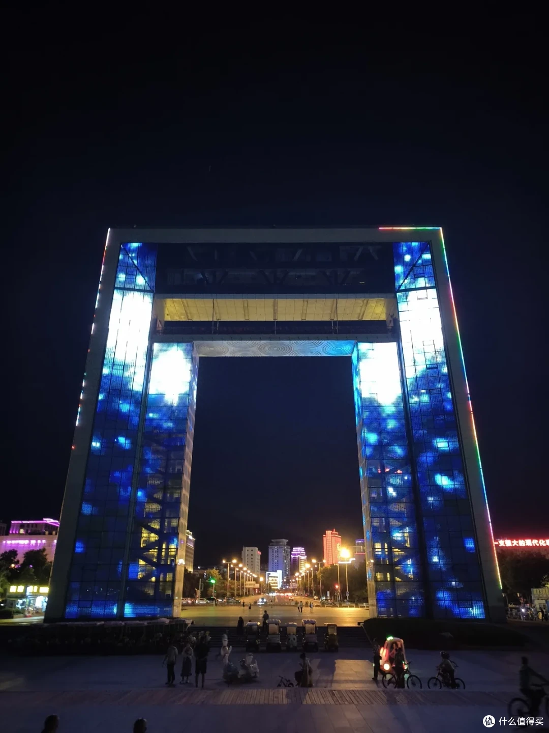 夜色中的幸福门通体亮着蓝色灯光，门洞里透出城市街道的灯火