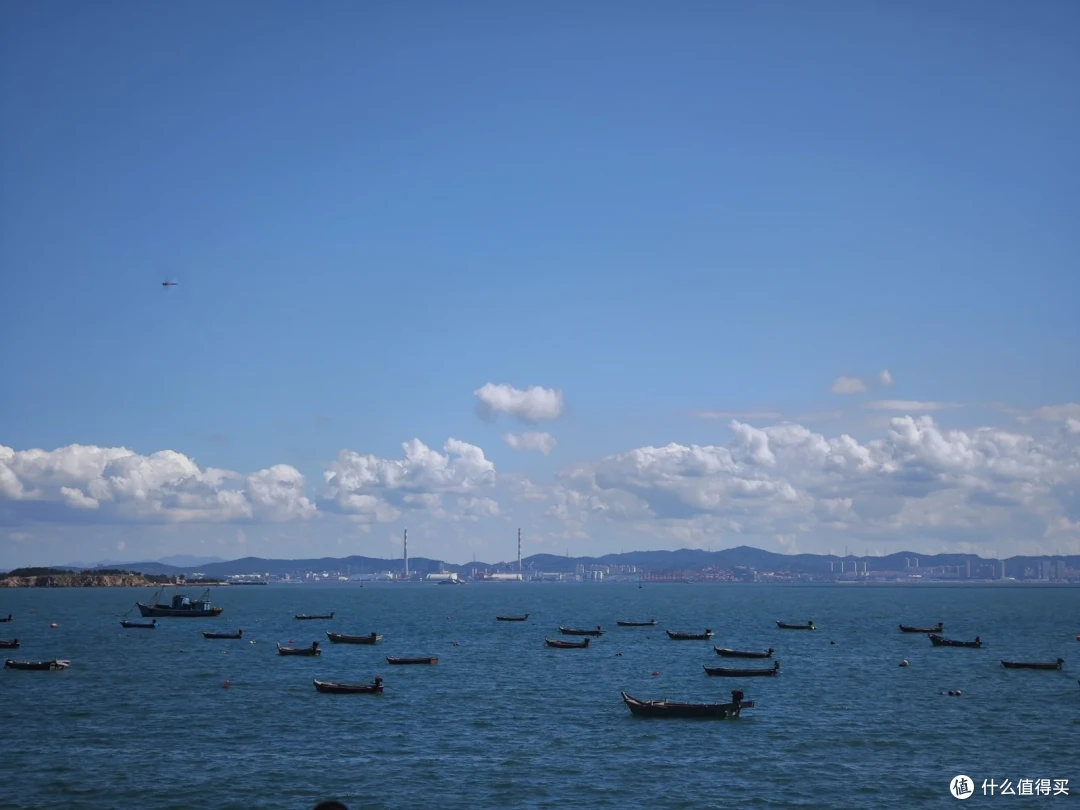 海源公园的海湾里泊满小舢板，对岸远处可见厂房烟囱与连绵山峦