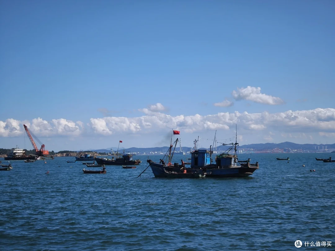 海源公园外的海面上泊着多艘插红旗的渔船，远处可见吊机船和沿岸城市
