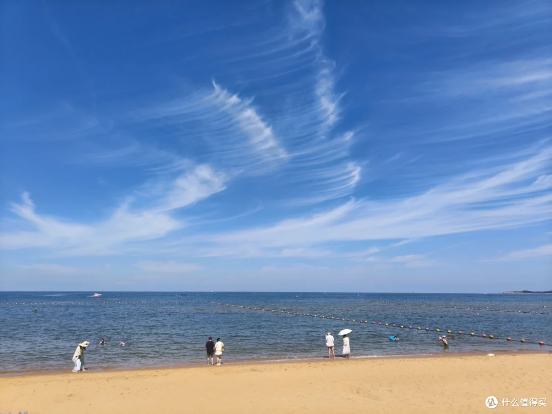 威海国际海水浴场，蓝天上铺开整齐的丝状卷云，沙滩上零星游客在水边散步
