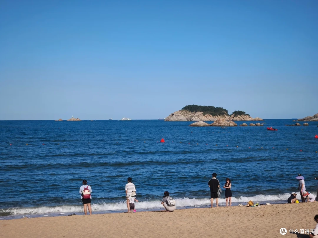 半月湾沙滩上游客踏浪玩耍，远处海中立着礁石小岛