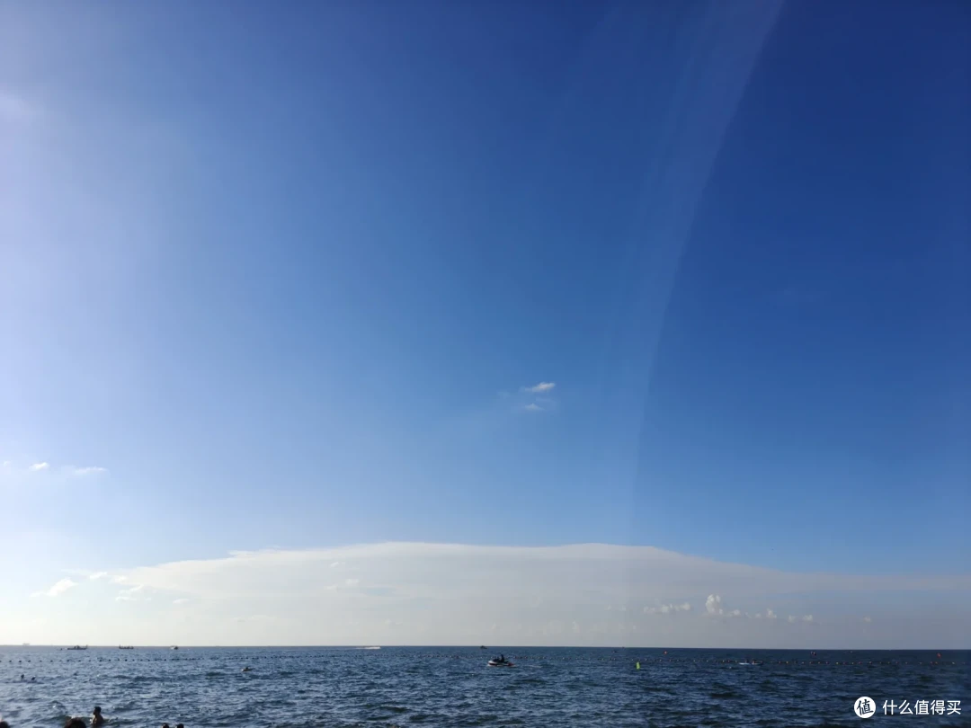 国际海水浴场的开阔海面，长云横过海平线，泳者与浮标散布水中