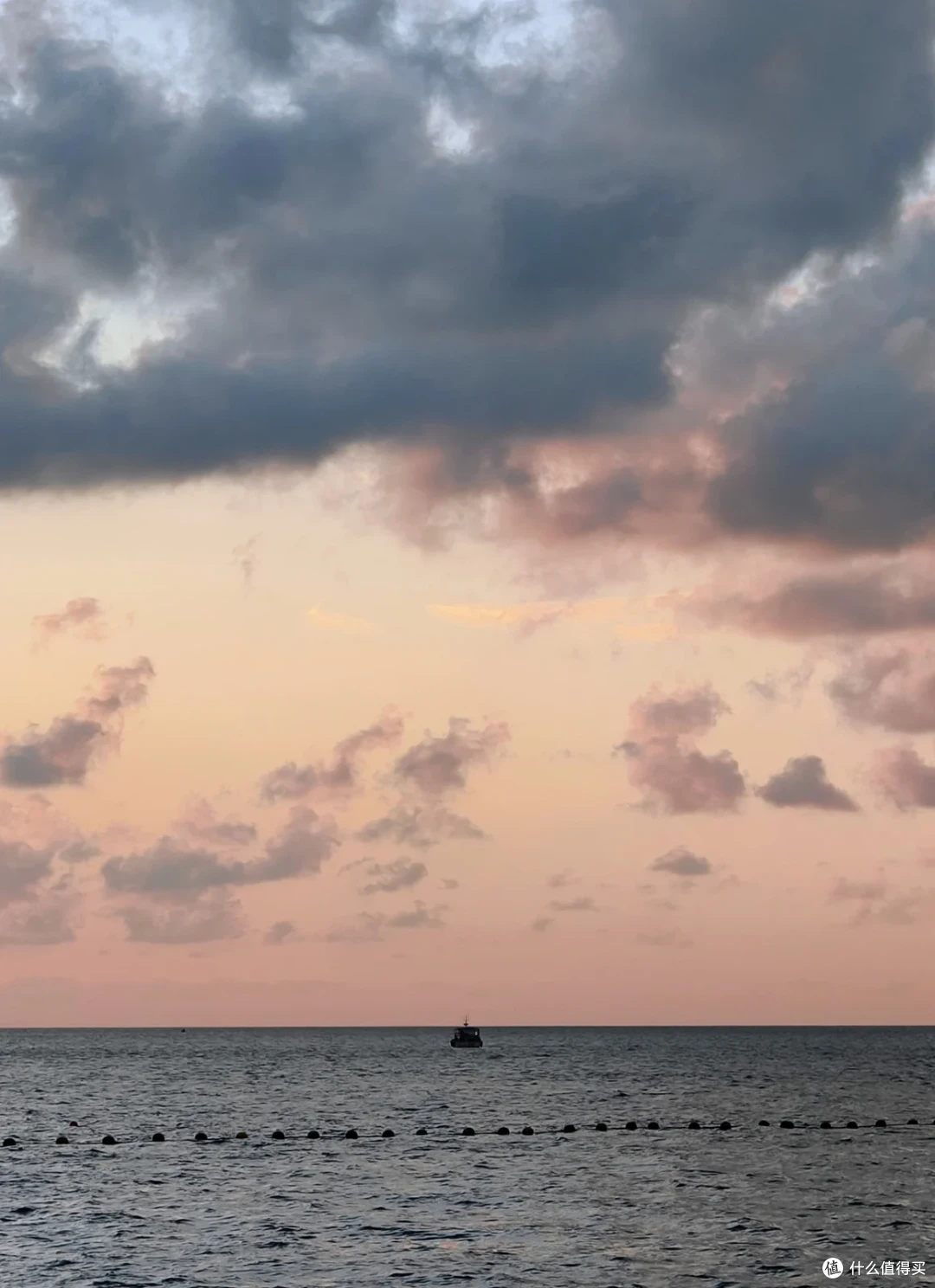 傍晚的国际海水浴场，粉橙色云层下远处漂着一艘小船