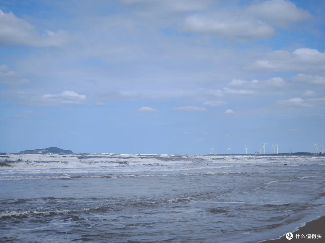 那香海海滩浪花朵朵，远处海岸线上立着一排白色风力发电机