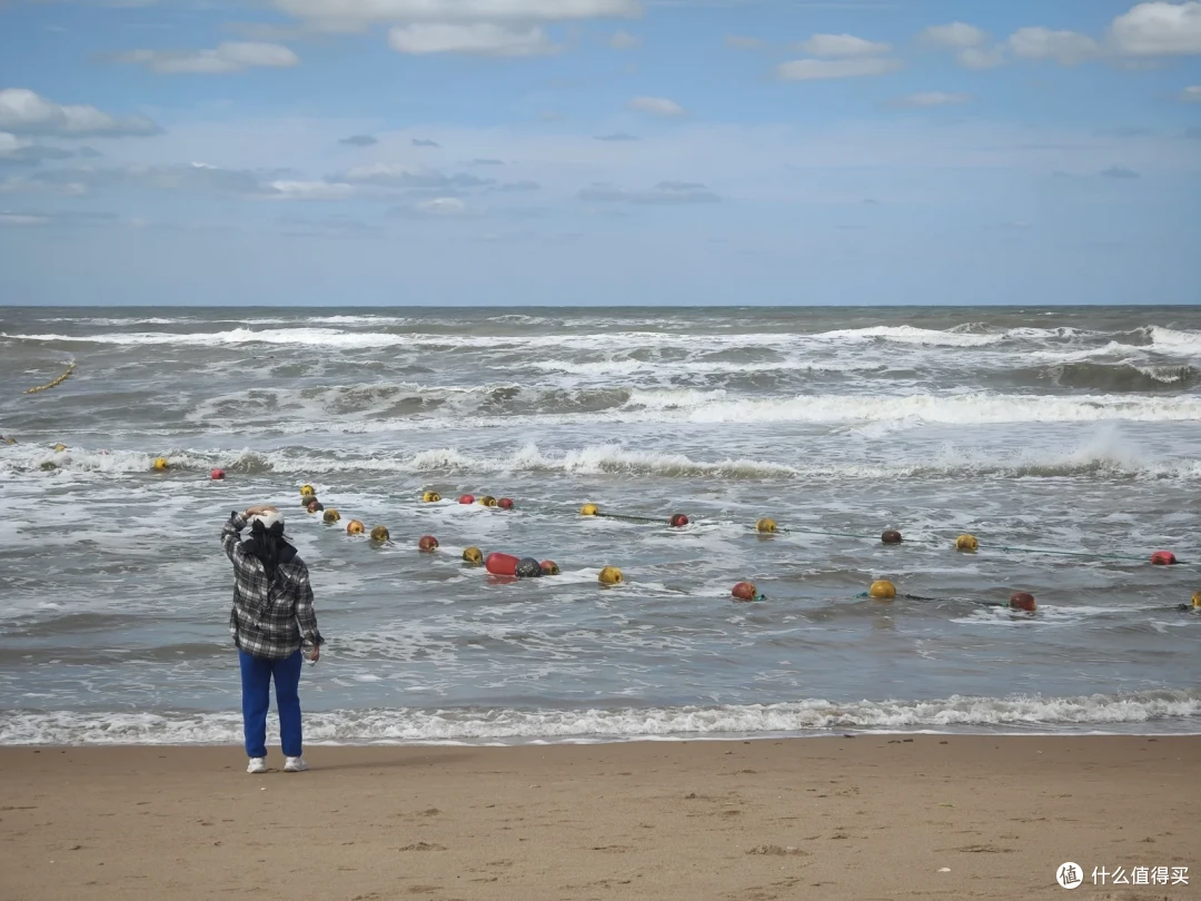 那香海海滩风浪大作，一名游客按着帽子呆立在岸边，近海漂着一串彩色浮球