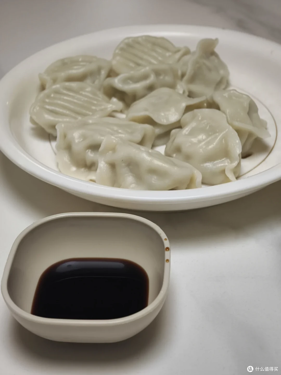 一盘皮薄馅饱满的鲅鱼饺子，旁边配一小碗深色蘸料