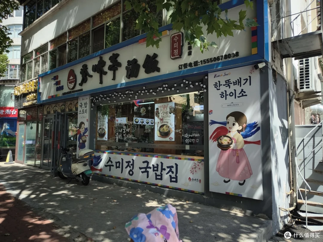 街边韩餐馆的招牌上中文与韩文并排，门口海报画着穿韩服端汤饭的女孩