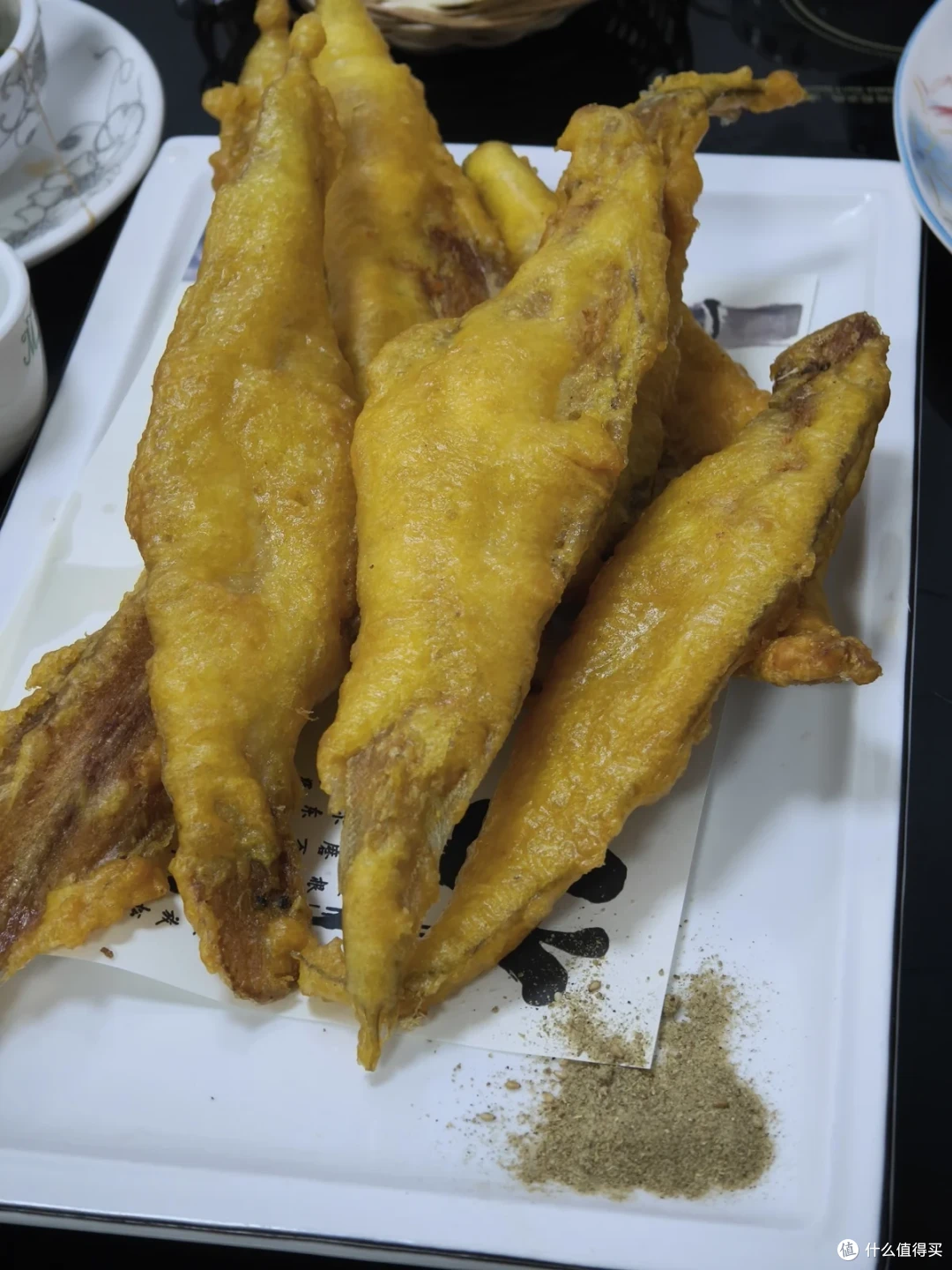 一盘金黄的油炸小鱼，细长鱼身码放在白瓷盘中，旁边一小堆椒盐