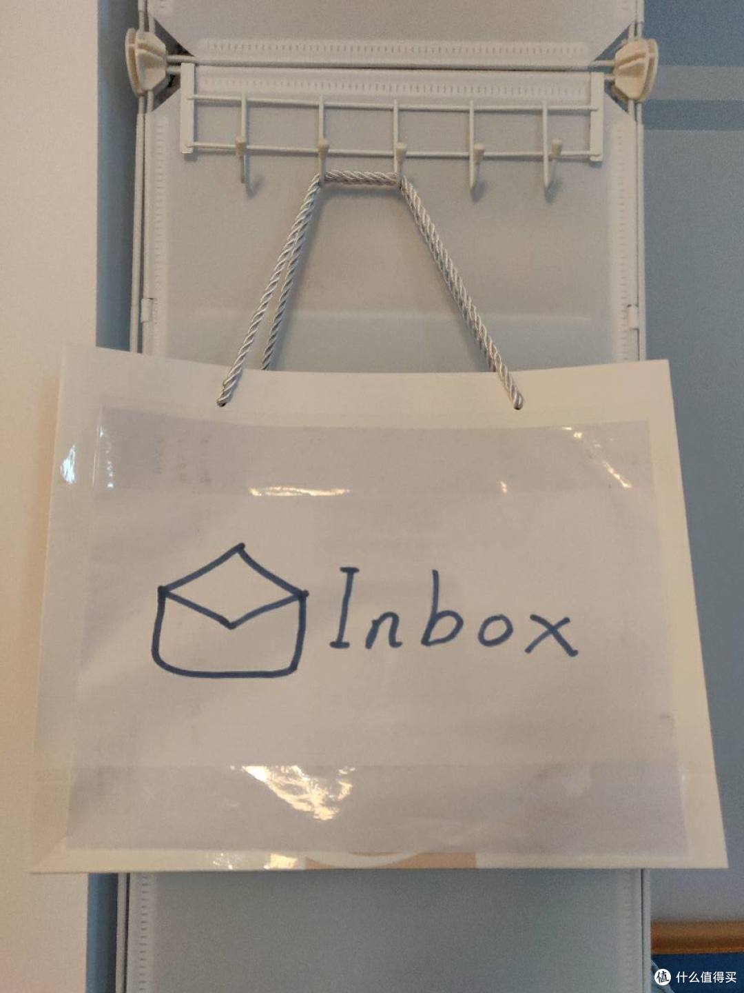 门后挂钩上挂着白色纸袋，袋面手写 Inbox 字样和信封图标，用来存放有时效性的纸质文件