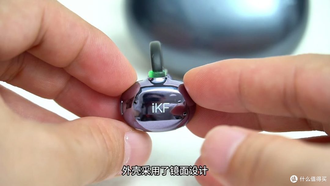 双手拿着单只耳机，外壳呈镜面反光，连接处亮起绿灯。
