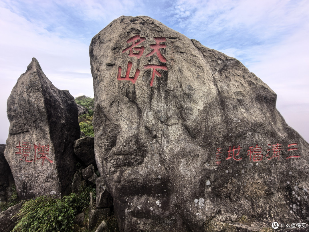 中央巨石上刻着醒目的红色大字“天下名山”，下方是“三清福地”；左侧较小的石头上则刻有“仙境”二字。这些石刻是对三清山自然风光和道教文化底蕴的高度赞誉。
