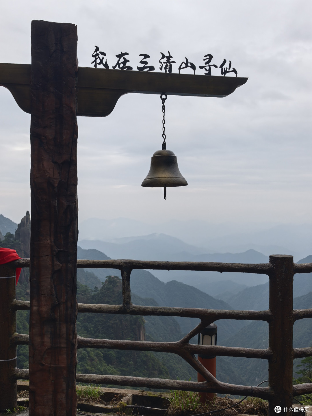 木牌写着“我在三清山寻仙”，配合悬挂的铜钟，营造出一种寻仙祈福的氛围。加上背景是典型的花岗岩峰林地貌，层峦叠嶂，云雾缭绕，非常契合三清山“天下第一仙峰”的美誉。