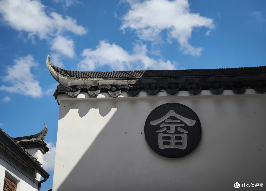 白墙上的黑底圆形牌匾，中间一个畲字，墙头是带滴水瓦的翘角屋檐
