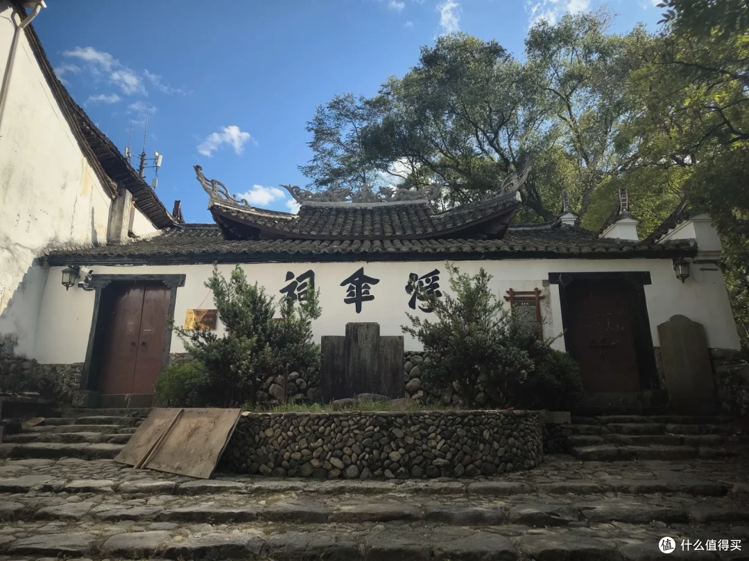 白墙黑瓦的祠堂式建筑，屋脊两端翘起，墙面题着三个墨色大字，门前是卵石台阶