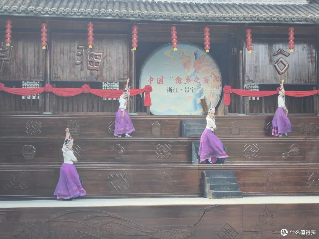 戏台上四位穿紫色长裙的舞者同时抬手起舞，背景圆牌上写着中国畲乡之窗