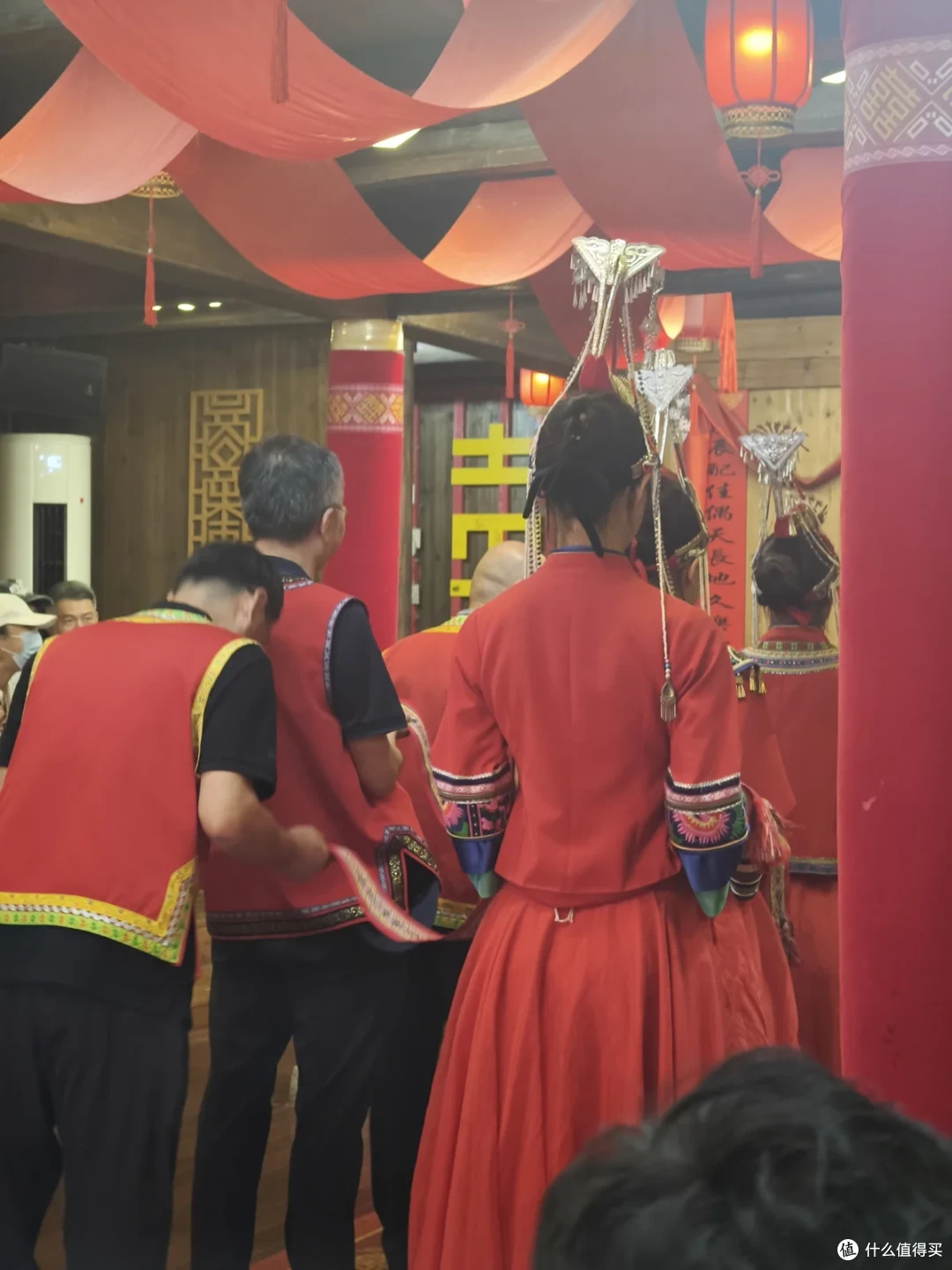 室内红色布幔下，几名穿红衣的演员聚在贴有囍字的厅堂里