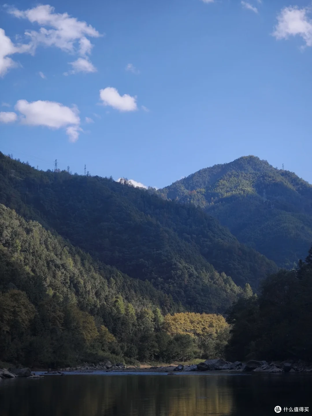 碧绿的溪水被两岸青山夹住，岸边一丛树叶已经转黄