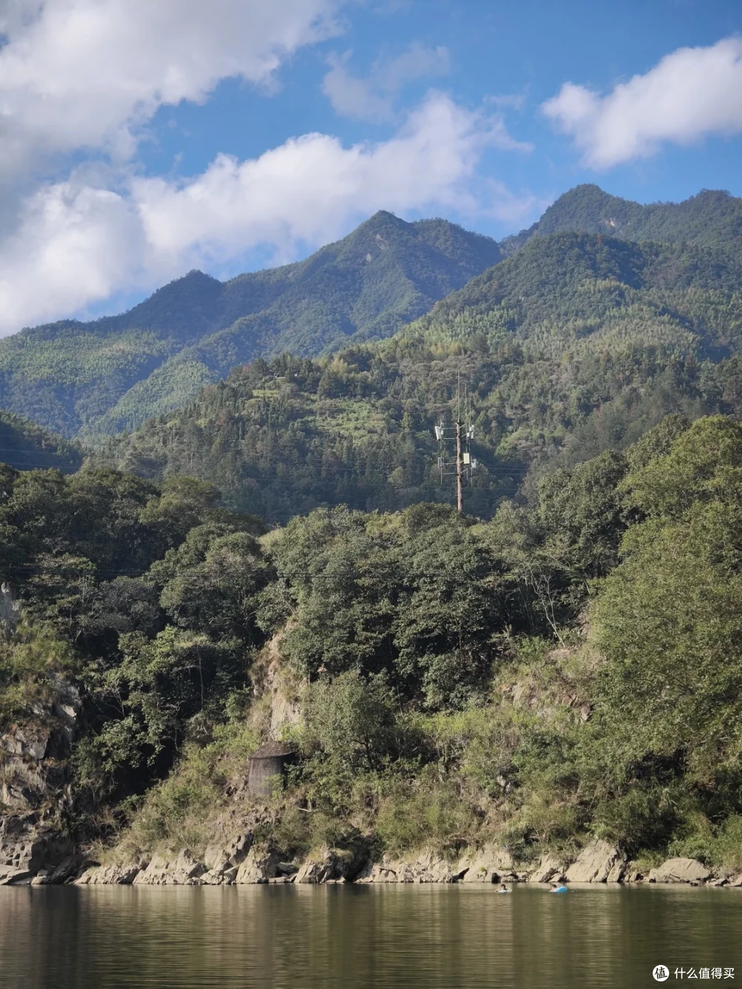 溪对岸林木覆盖的山坡，坡上立着一座通信铁塔，山脚有石砌小棚