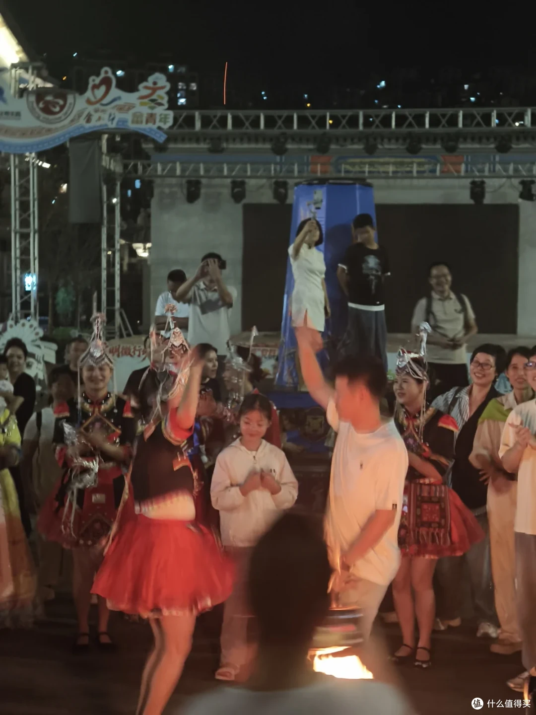 夜间舞台前，演员与游客围成圈跳舞，一旁有女孩驻足观看