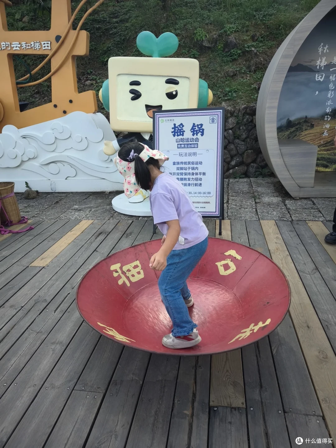 小女孩站在红色圆盘上，旁边立着摇锅的说明牌和卡通立牌