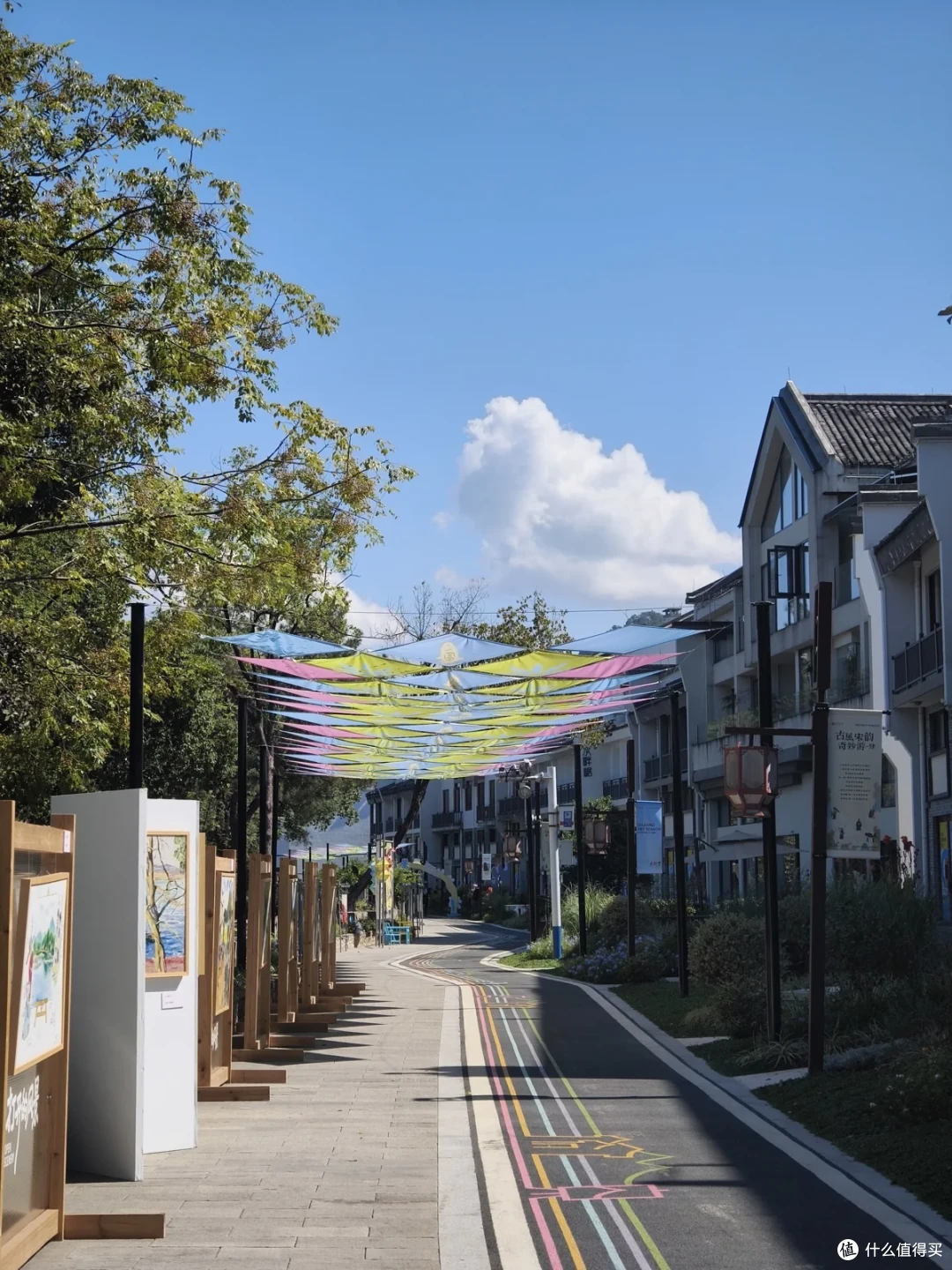 江边街道上方拉着彩色布条，两侧摆着展板和画廊招牌