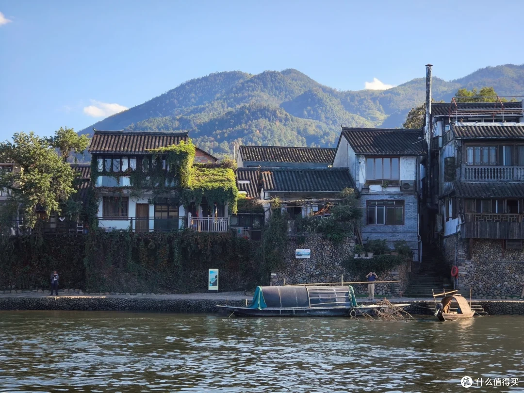 沿江的白墙民房与停泊的小船，背后是青山