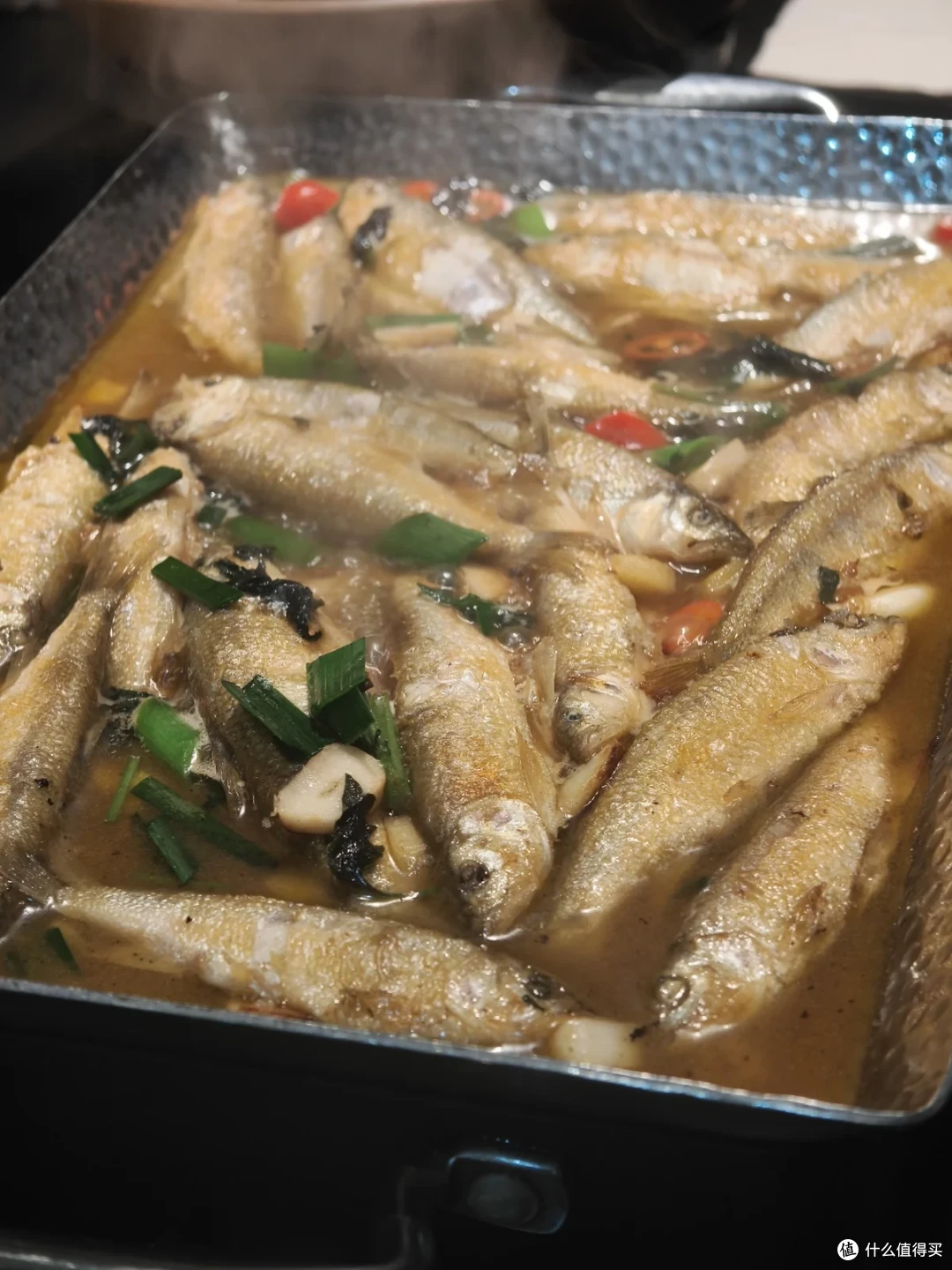长方铁盘里码满红烧小溪鱼，汤汁里漂着葱花和辣椒